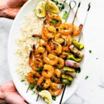 Overhead image of grilled skewered shrimp on a platter of rice with a side of watermelon salsa.