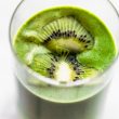 close up image of superfood smoothie in a cup topped with kiwis.