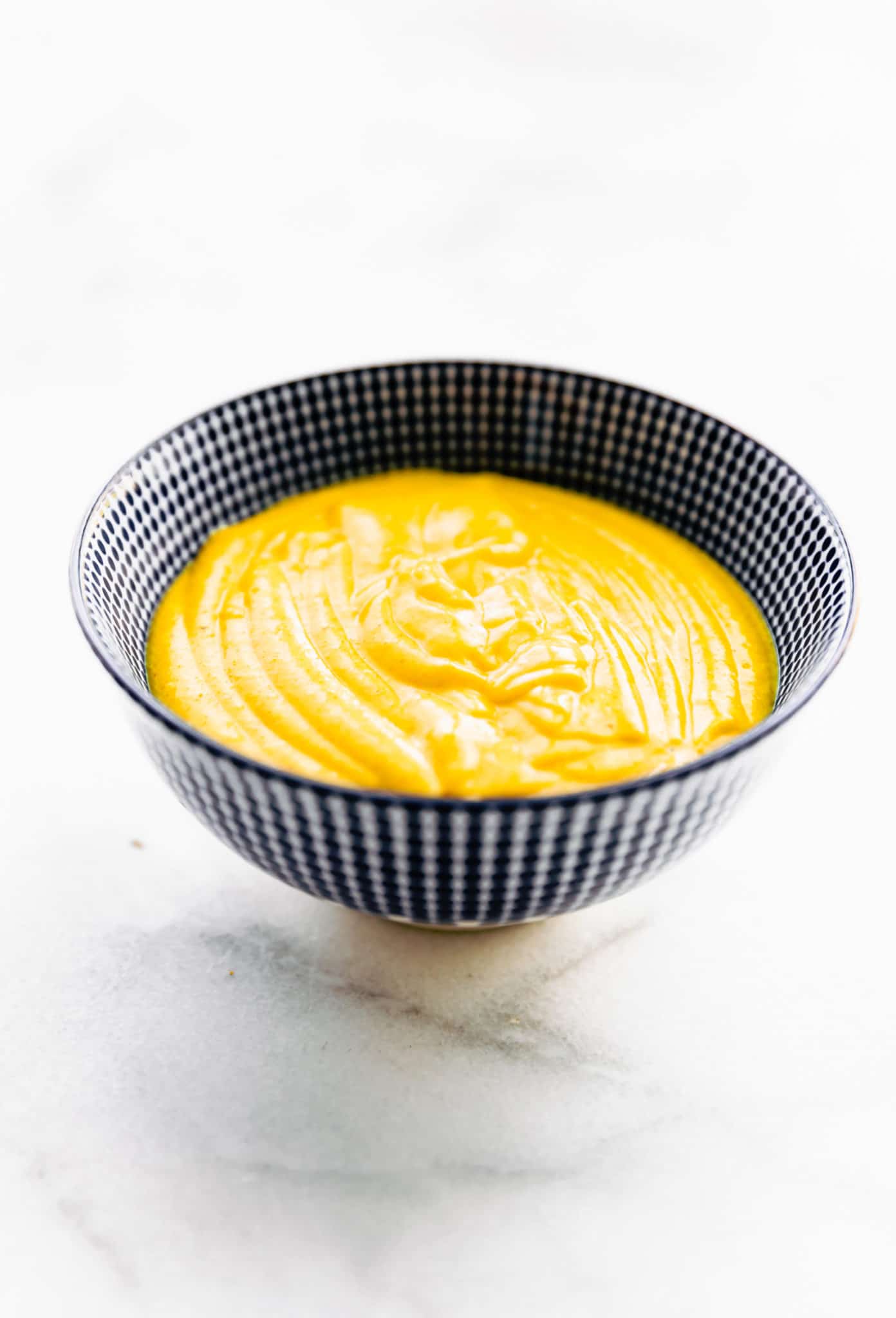 Vegan cheese sauce in a blue bowl on a white tabletop.