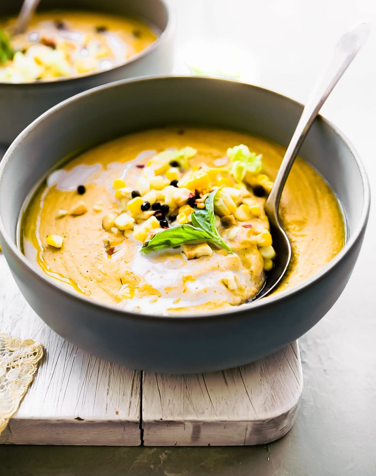 Roasted corn soup in a black bowl topped with roasted corn kernels, a spoon scooping up a bite.