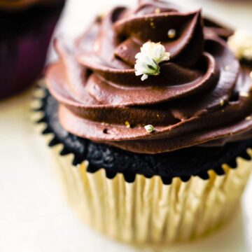 Up close photo of a chocolate cupcake topped with chocolate frosting and a white flower.