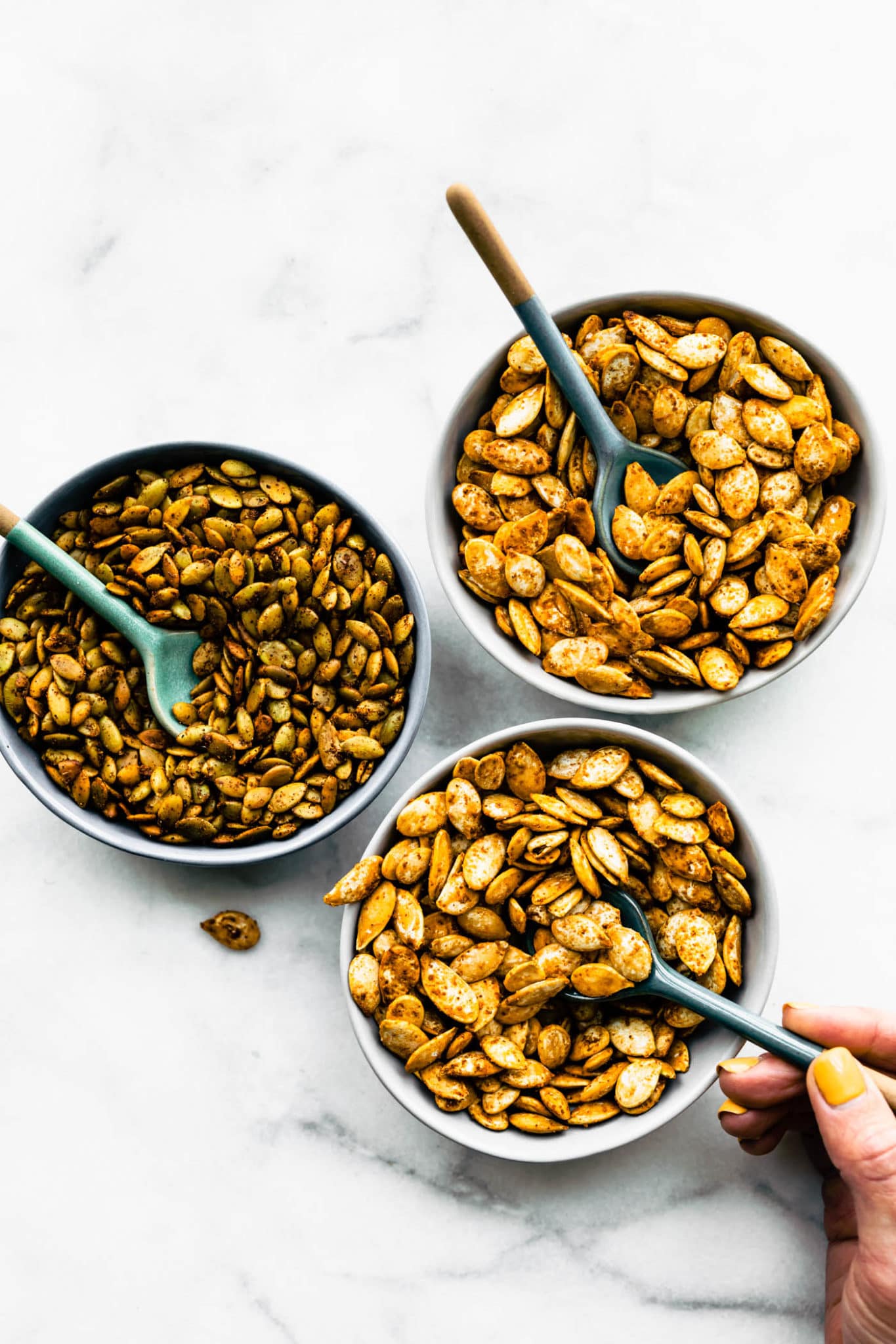 3 bowls of pumpkin seeds flavored different ways with spoons