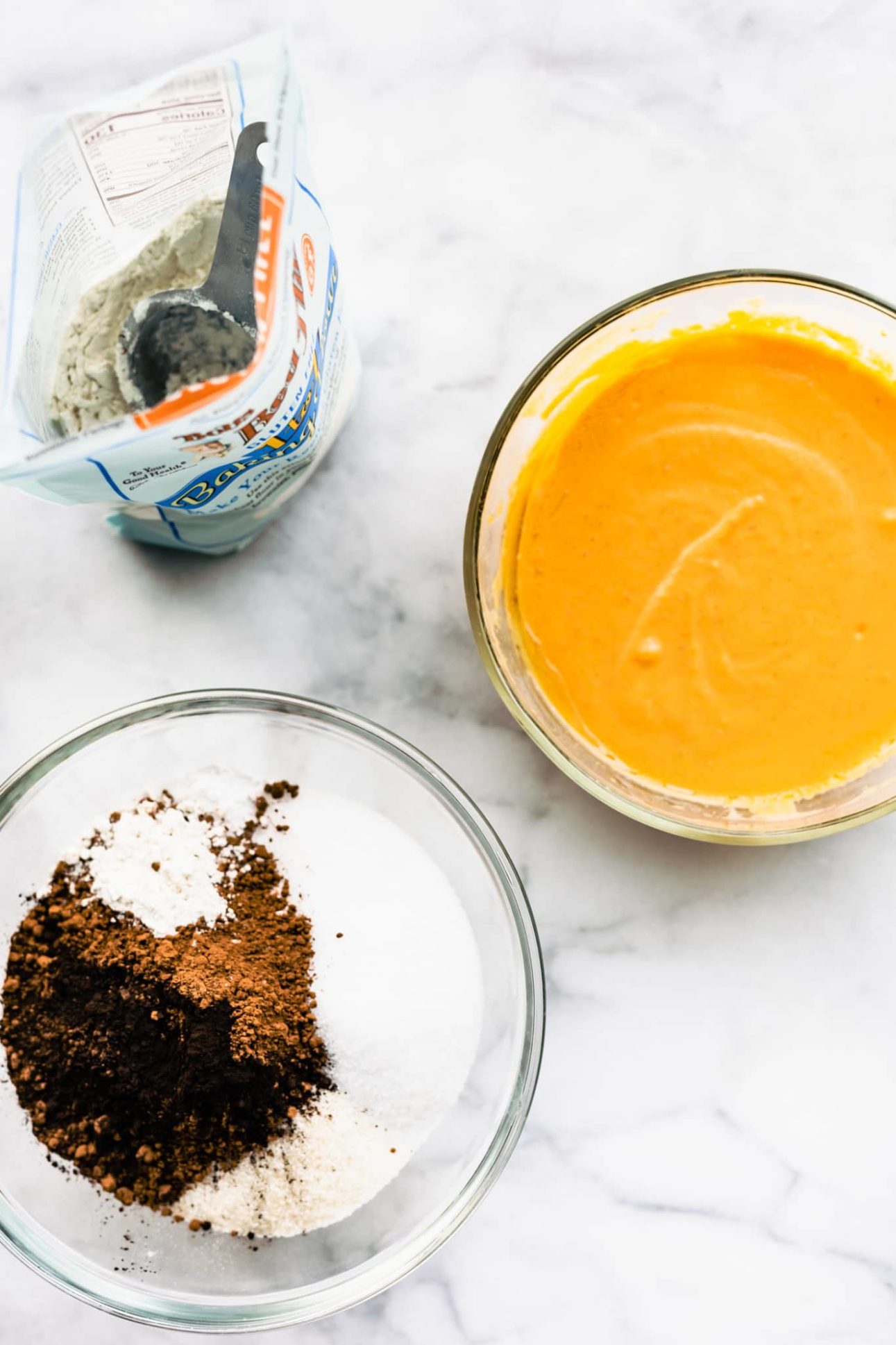 overhead shot of dry flour batter in one bowl and wet batter with pumpkin puree in another bowl for a vegan chocolate cupcake recipe