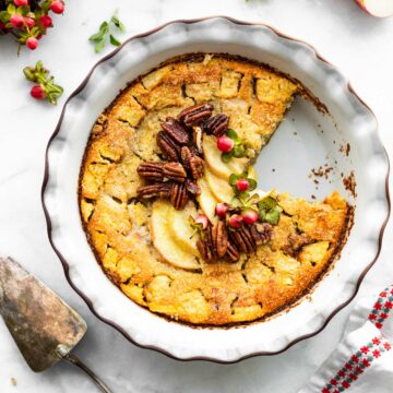 Gluten free apple pie in a white pie pan with a slice taken out topped with sliced apples and whole pecans