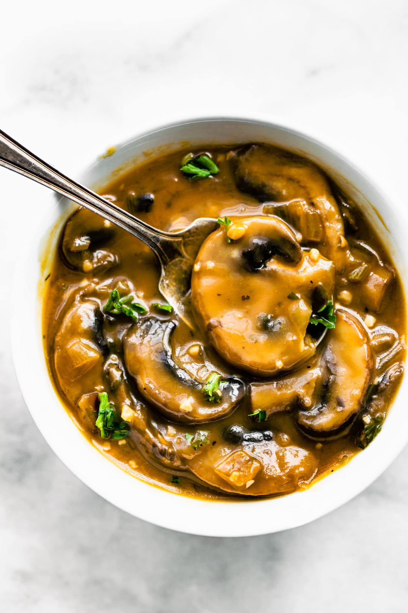 overhead shot of vegan mushroom gravy in a small white bowl with spoon in gravy.