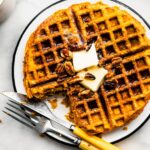 Gluten free sweet potato waffle with a bite taken out topped with butter on a plate with a knife and fork
