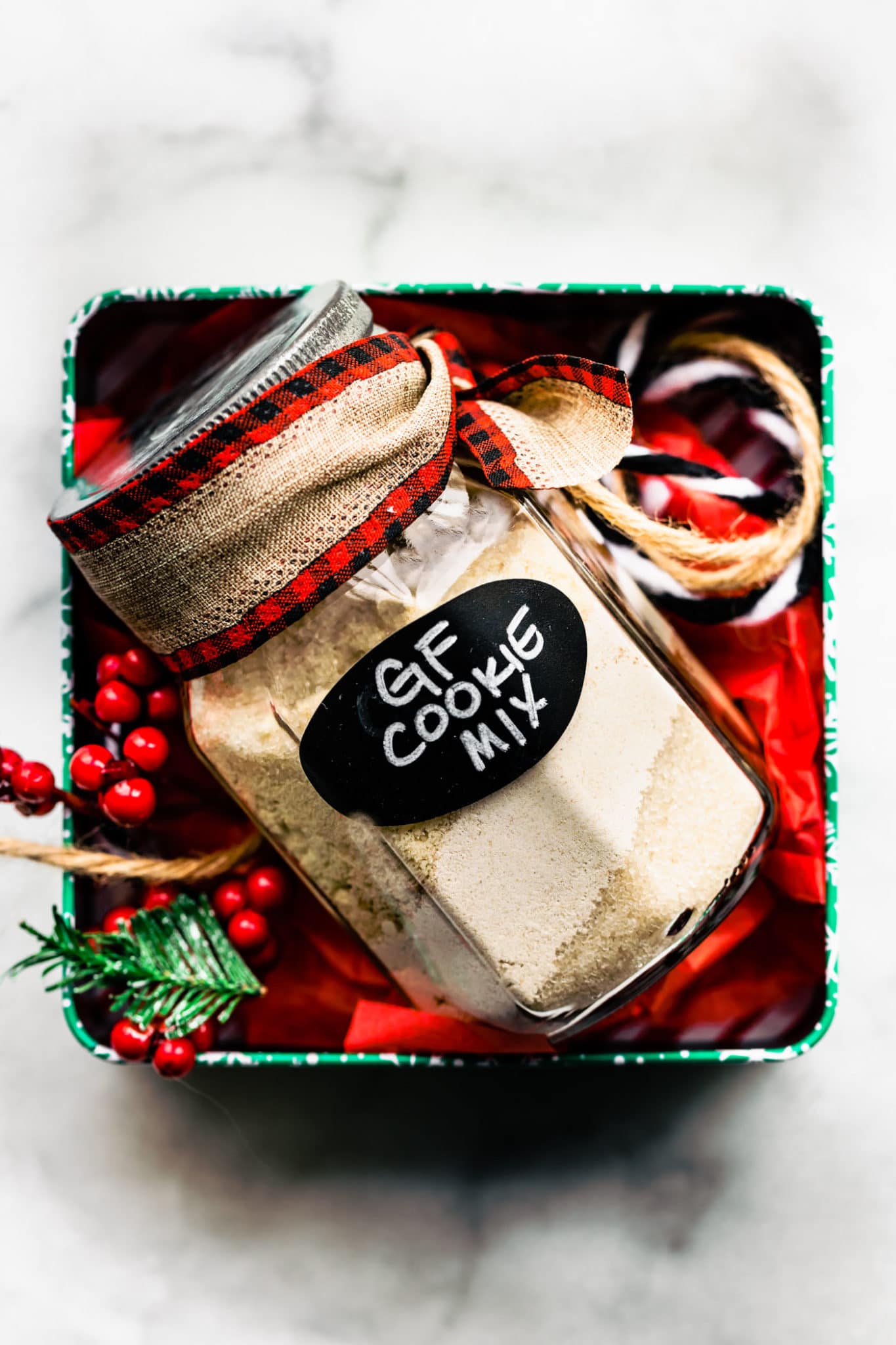 Gluten free cookie mix in a jar in a box with red tissue paper and cranberries