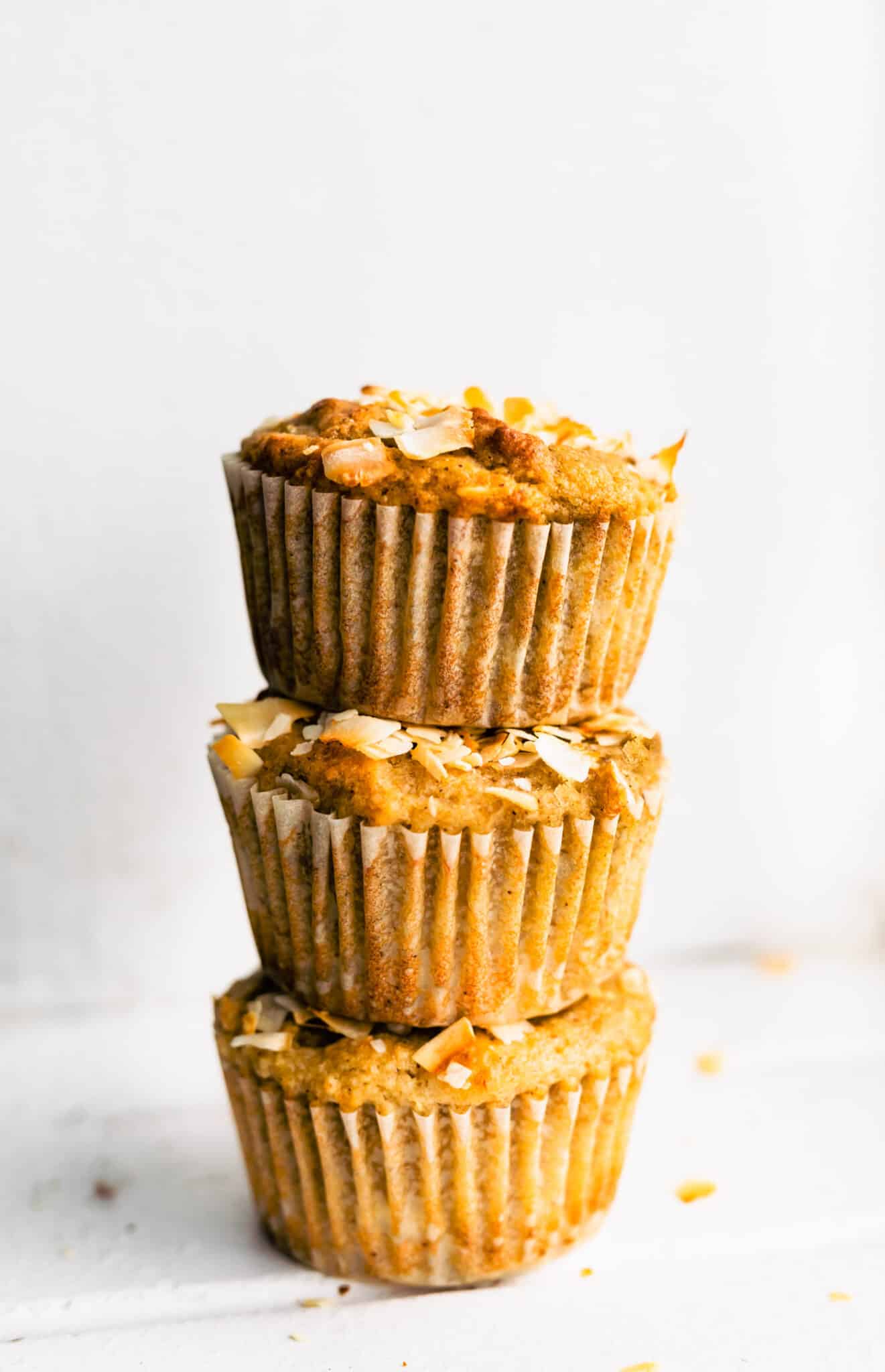 three almond flour banana muffins with coconut stacked on top of each other