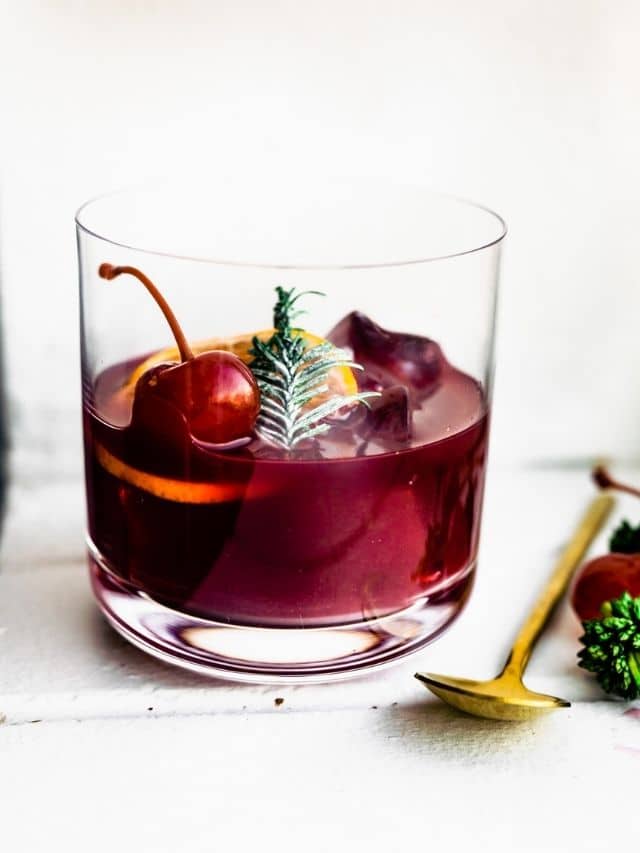 A short glass half filled with Yuletide Red Wine Cocktail garnished with orange slice and cherry.