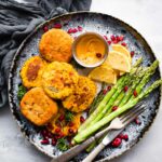 salmon cakes on a plate with asparagus and a dipping sauce