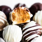 a side image of a carrot cake ball with a bite taken out of it sitting on top of other cake balls that have been coated with white and dark chocolate