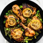 4 thighs and 2 drumsticks of honey ginger air fryer chicken in a pot on top of air fried asparagus topped with lemon slices and green onions