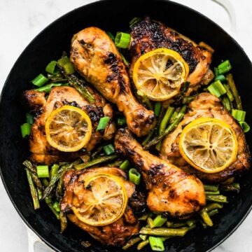 4 thighs and 2 drumsticks of honey ginger air fryer chicken in a pot on top of air fried asparagus topped with lemon slices and green onions