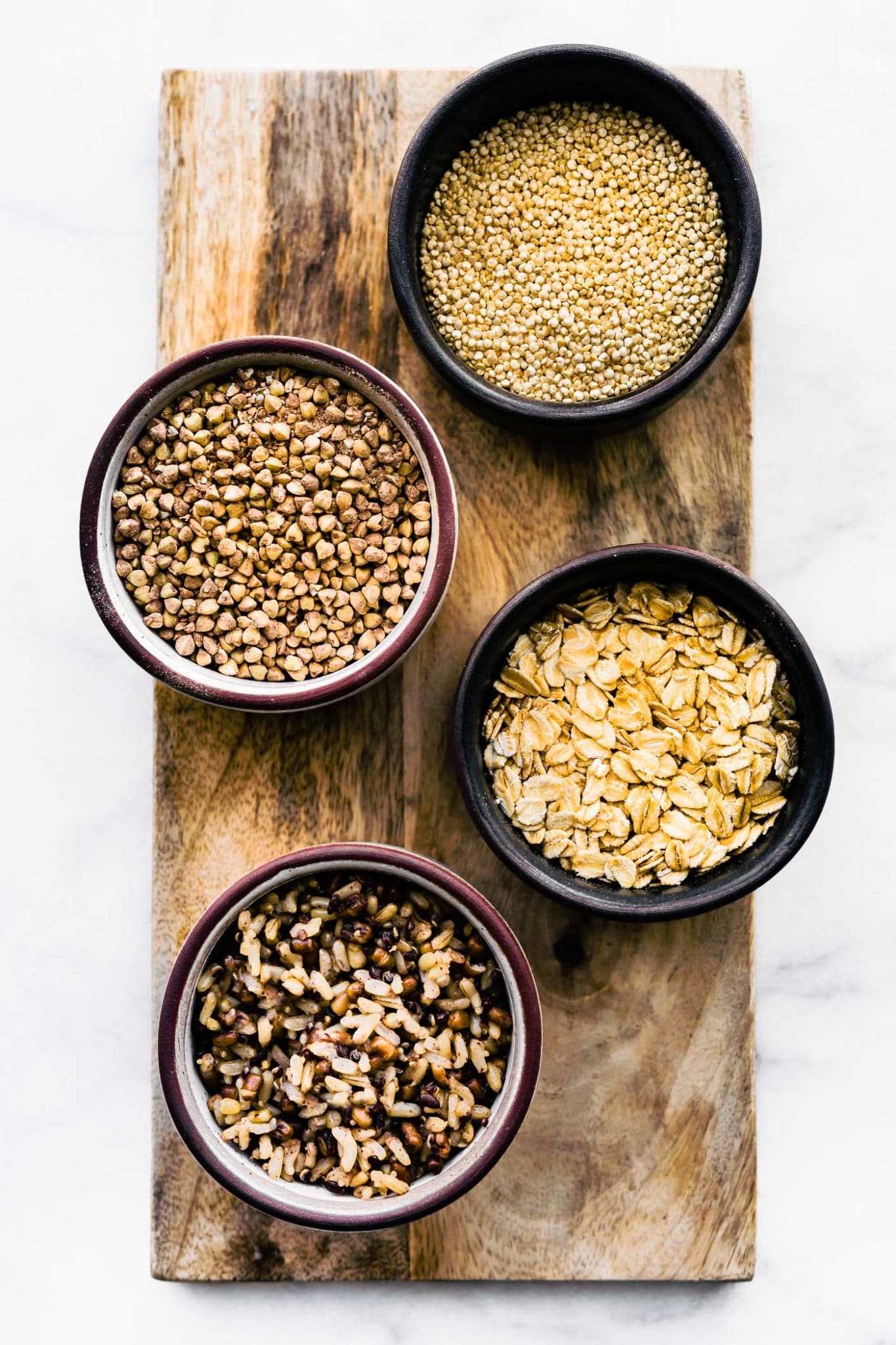 four bowls of gluten free grains on a wooden plank containing buckwheat, millet, gluten free oats, and quinoa