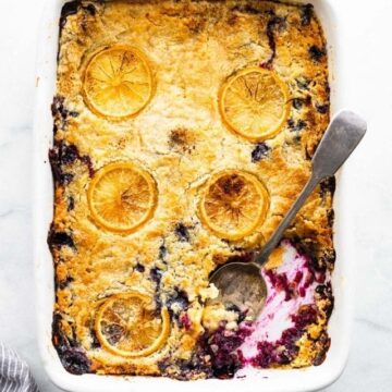 Overhead view of 5-Ingredient Lemon Blueberry Cake in a white cake pan with lemon slices baked into the golden topping.