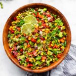 a wooden bowl full of fiesta quinoa salad made with lettuce, quinoa, bell peppers, corn, and cilantro topped with two lime slices