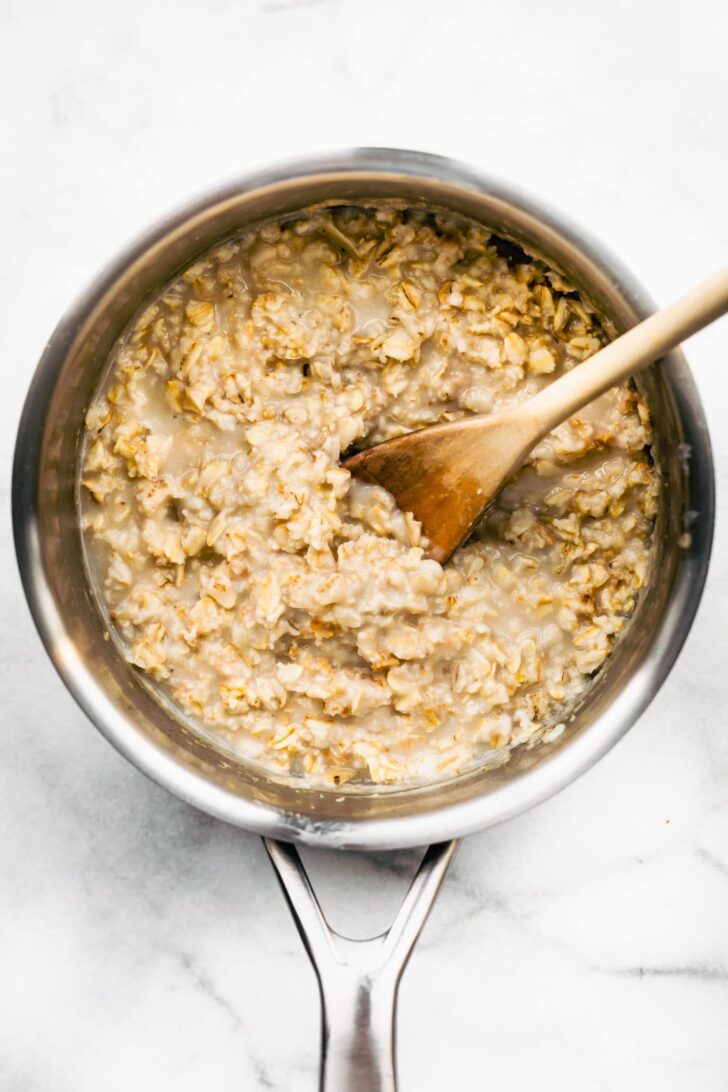 a sauce pot full of cooked rolled oats with spoon in middle