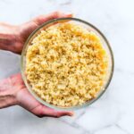 two hands holding a glass bowl full of gluten free quinoa grains
