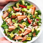 two hands holding a white bowl full of the best summer strawberry salad recipe