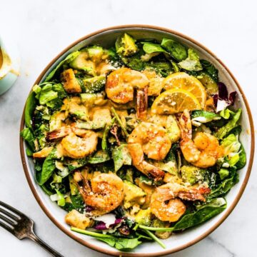 Overhead view spicy shrimp caesar salad in white bowl with brown rim.