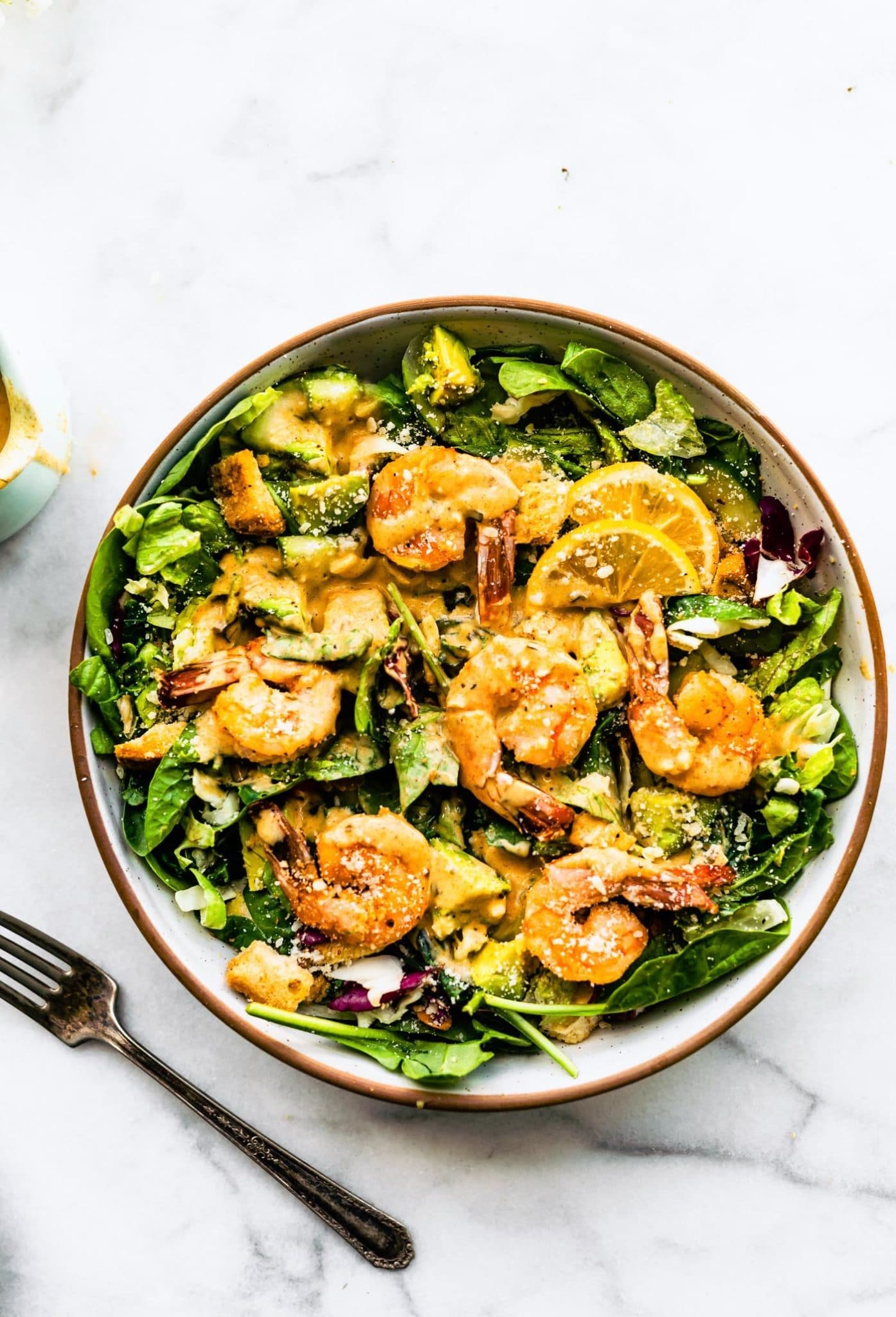 Overhead view spicy shrimp caesar salad in white bowl with brown rim.