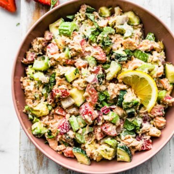 a bowl of strawberry salmon salad topped with a lemon wedge
