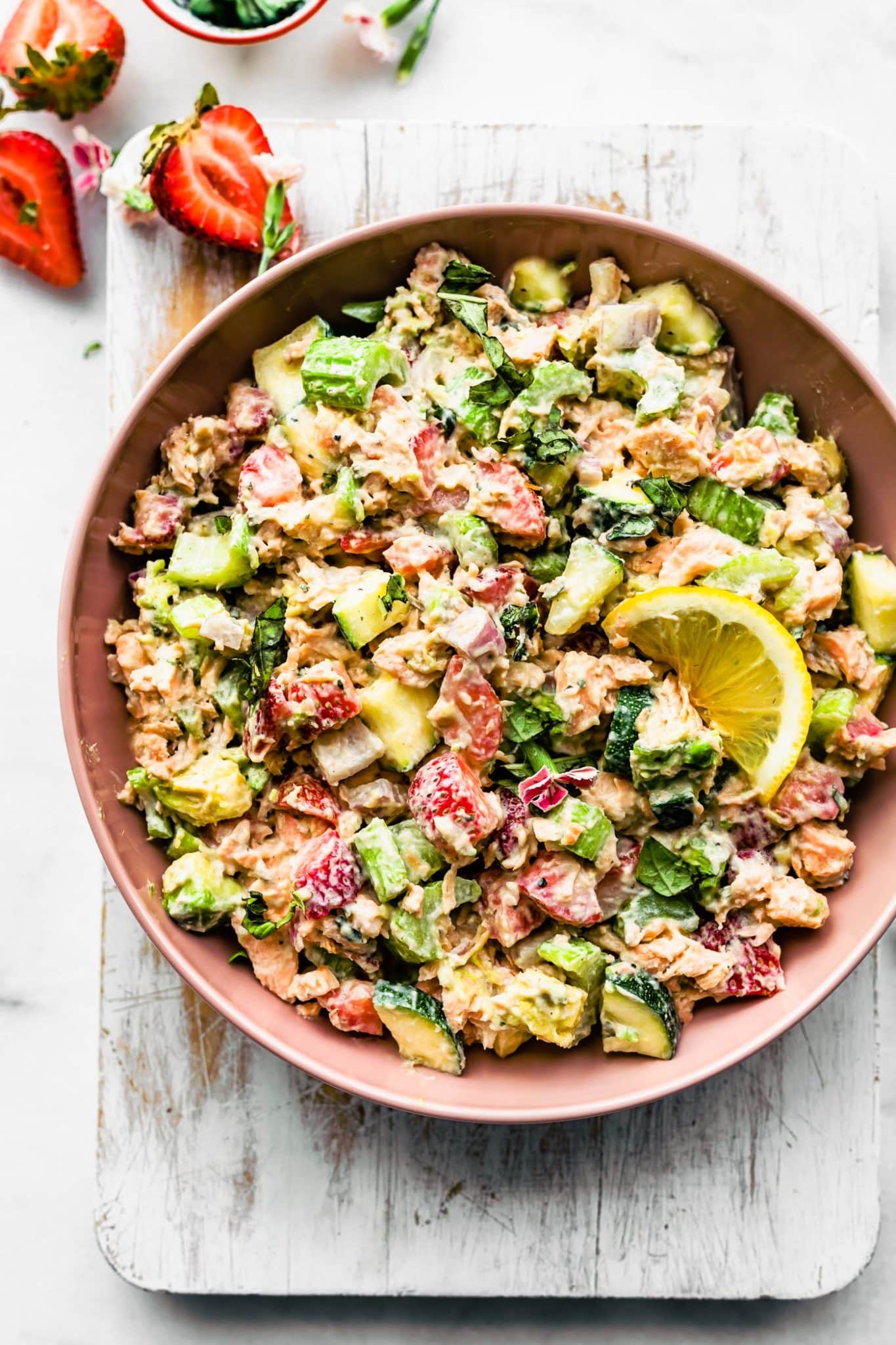 a bowl of strawberry salmon salad topped with a lemon wedge