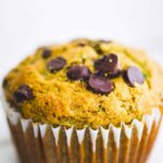 a close up image of a dairy free gluten free zucchini muffin with chocolate chips in a white muffin liner