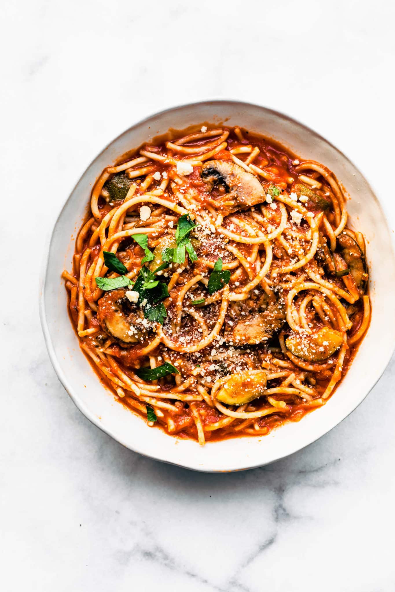 overhead image of a white bowl full of gluten free slow cooker spaghetti with mushrooms topped iwth fresh herbs