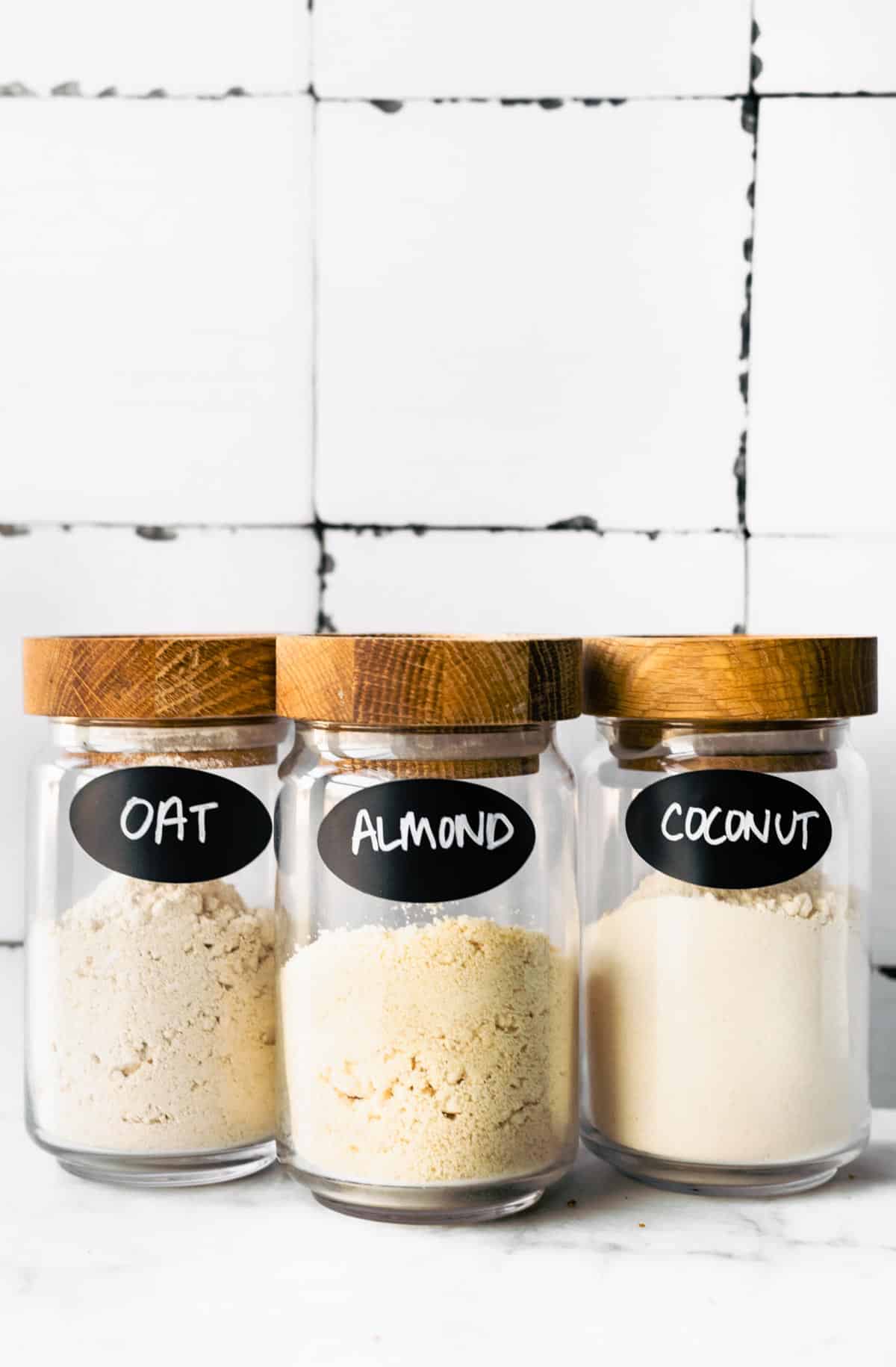 three glass jars full of gluten free flours including oat flour, almond flour, and coconut flour