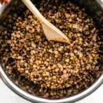 Brown lentils being stirred in a pot with a wooden spoon.