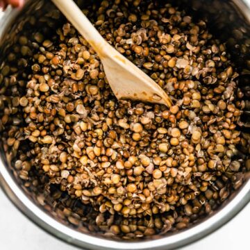 Brown lentils being stirred in a pot with a wooden spoon.