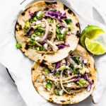 Two mojo pork tacos with lime wedges on the side.