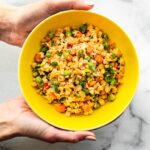 Hands holding a bowl of Cauliflower Fried Rice.