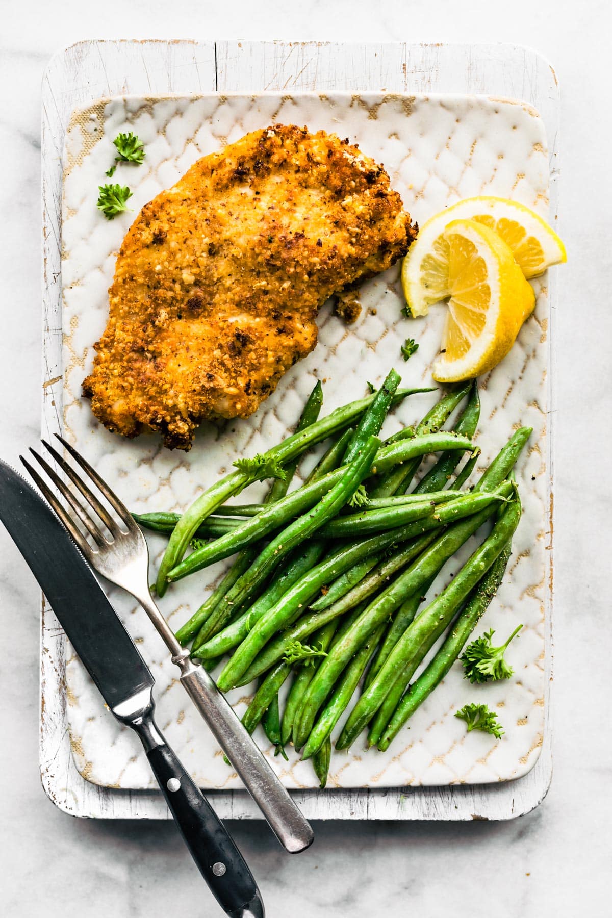 Gluten-Free Panko Chicken breast on a plate with green beans and a lemon wedge.