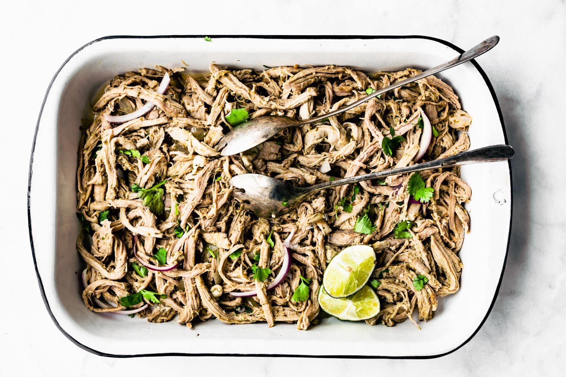 shredded pork in white casserole dish with 2 serving utensils on top