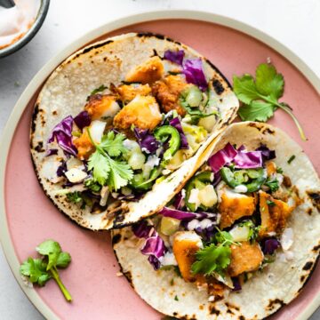 A plate of two gluten-free air fryer fish tacos topped with pineapple slaw, jalapeño slices, and cilantro.