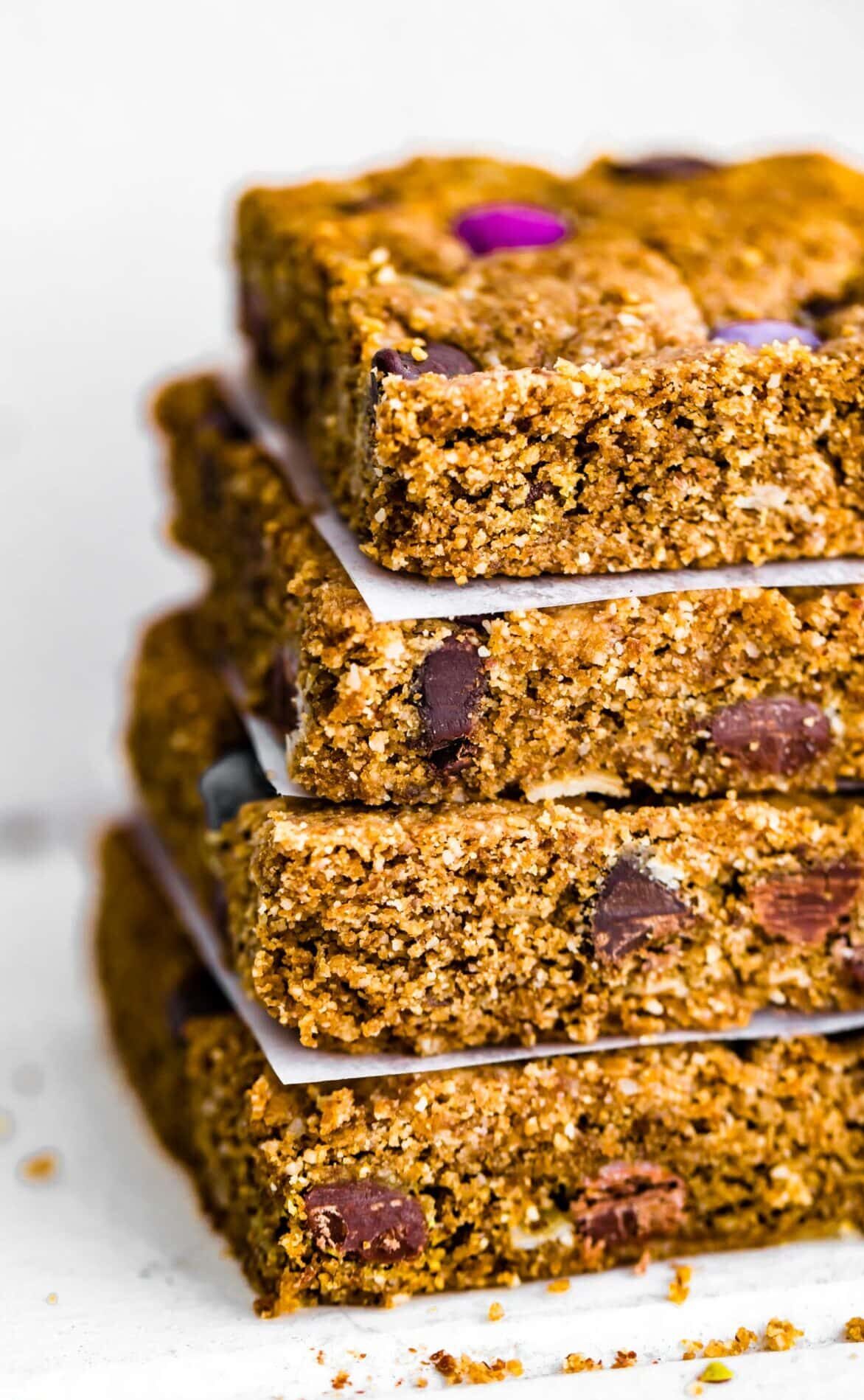 Four gluten free monster cookie bars stacked on top of each other with parchment paper in between each piece.