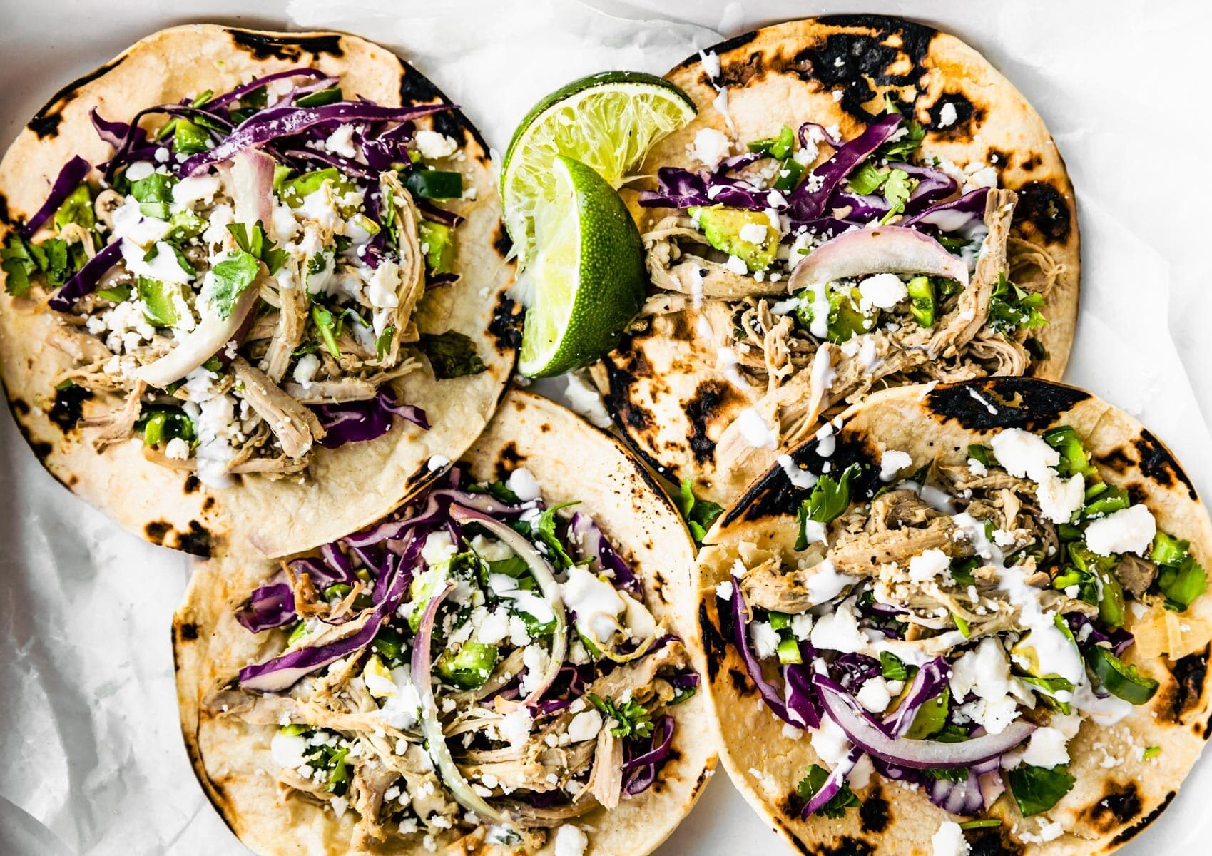 4 pork tacos with red cabbage and cilantro on top. Lime on side. Sitting on a parchment paper