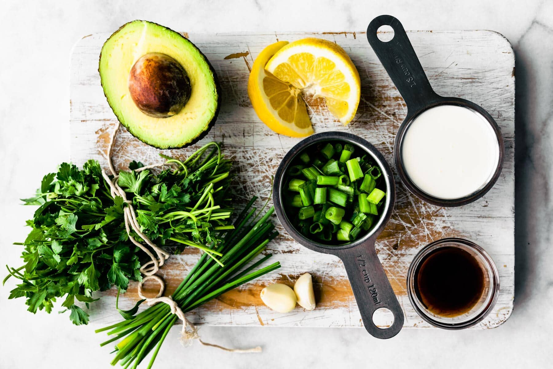 Fresh herbs, garlic, scallions, non-dairy milk, maple syrup, lemon wedges, and an avocado.