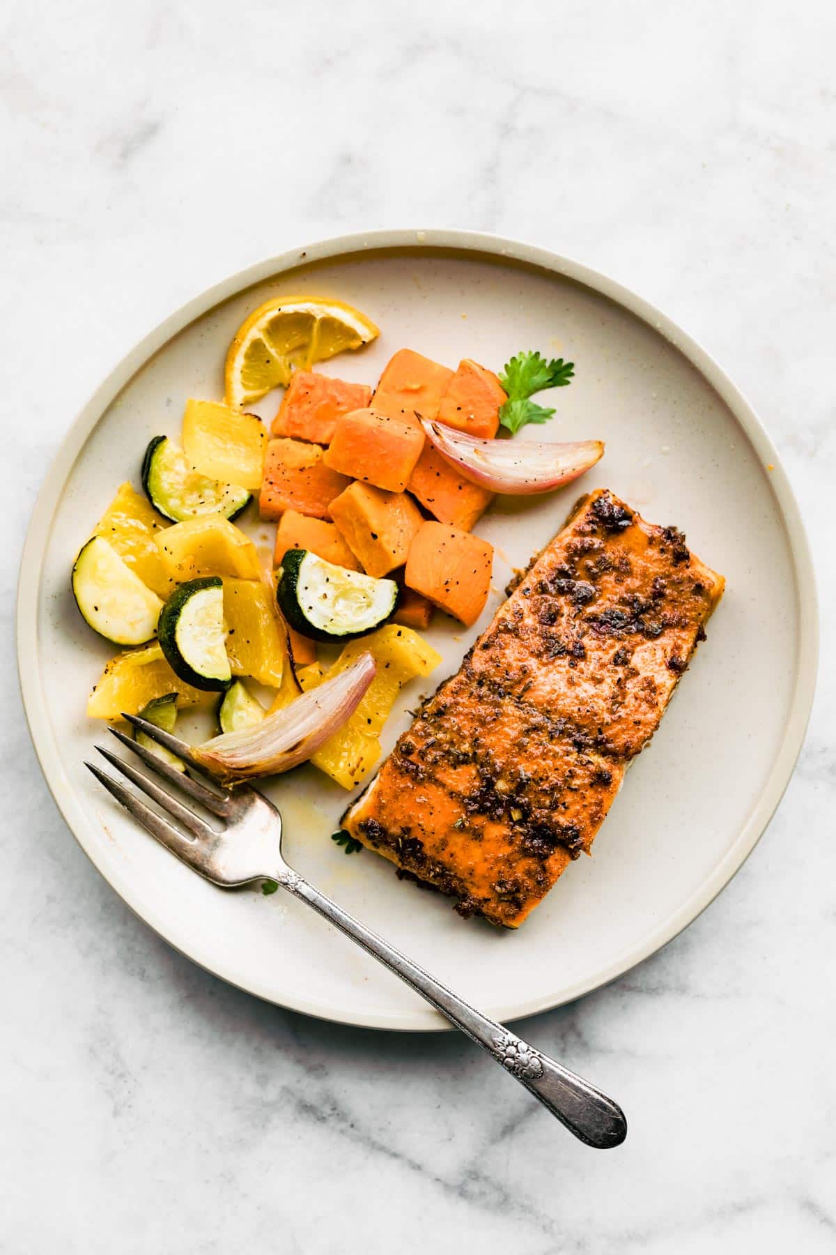 An overhead view of a white plate with baked jerk salmon and roasted veggies.