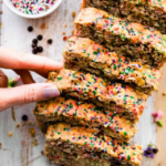 Sliced vegan ice cream bread with sprinkles and a woman's hand reaching for a slice.