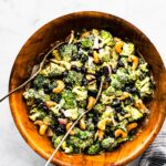 A creamy no mayo broccoli salad in a wooden bowl with two spoons.