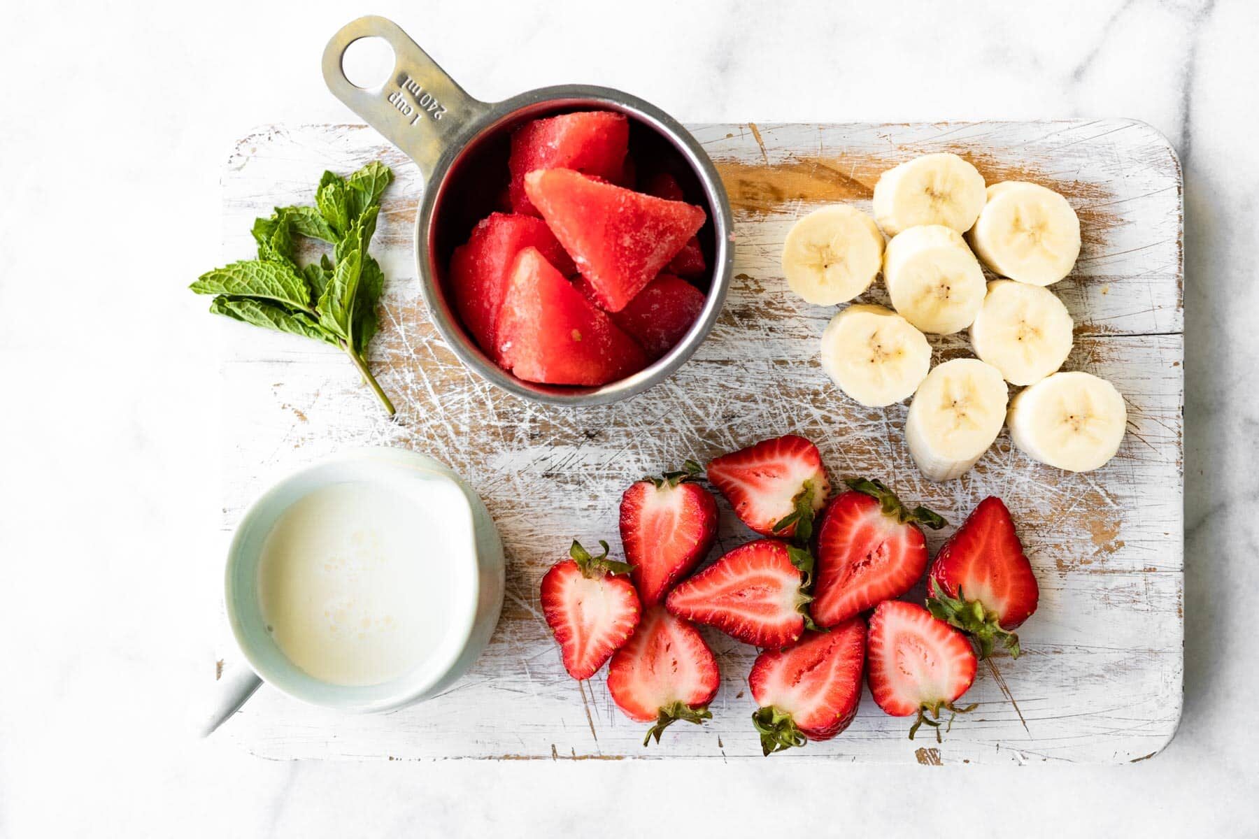 Frozen watermelon, halved strawberries and banana coins on a white cutting board.
