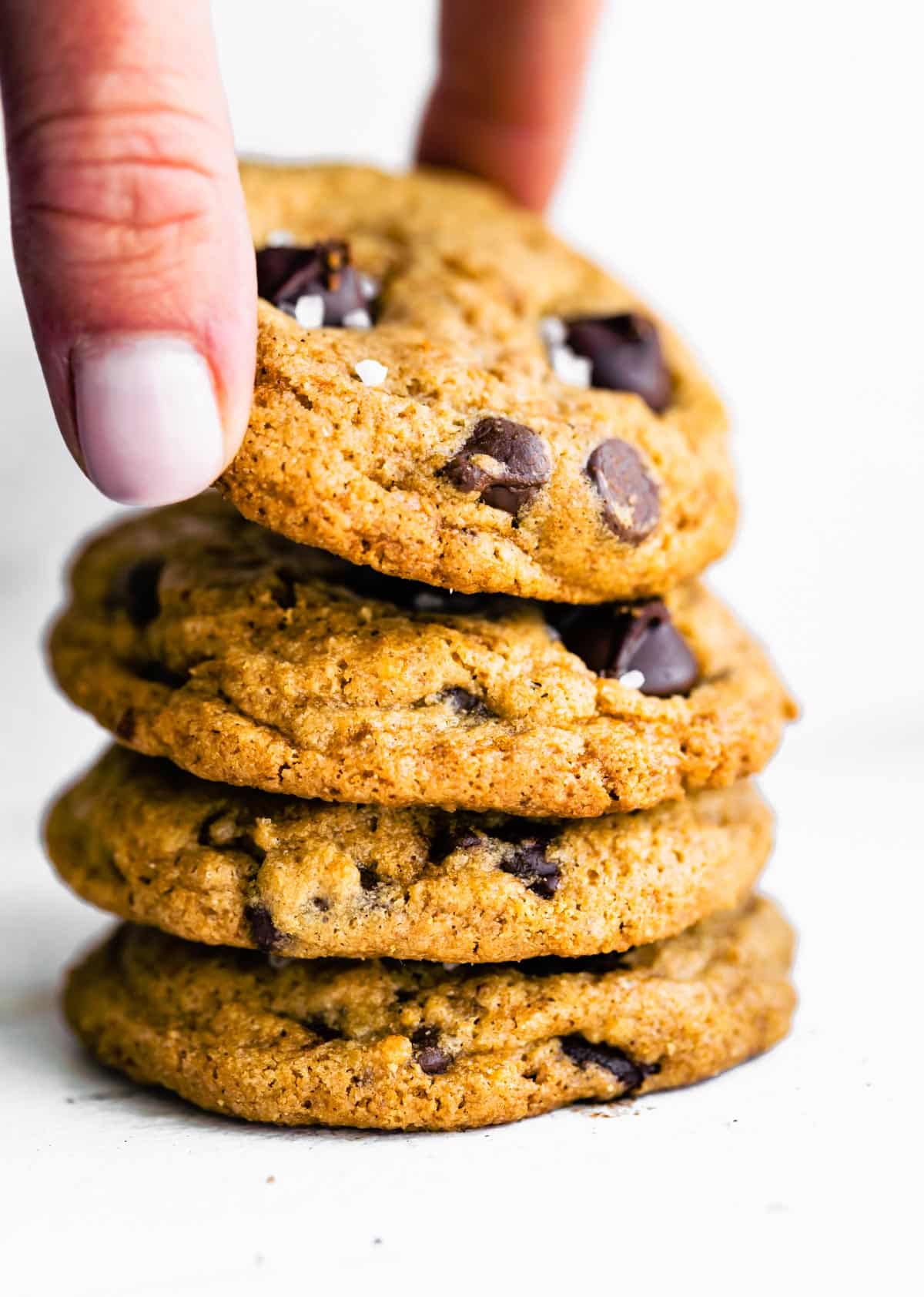 A woman's hand picking up a chocolate chip cookie from a stack of cookies.