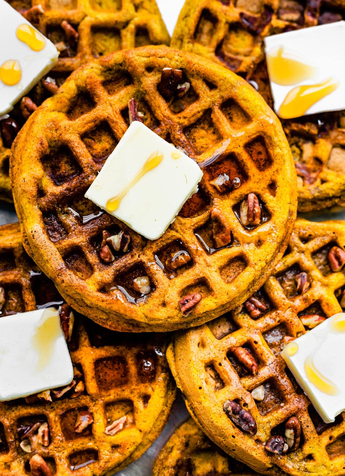 Overhead photo of pumpkin waffles on top of each other with butter, syrup and pecans.