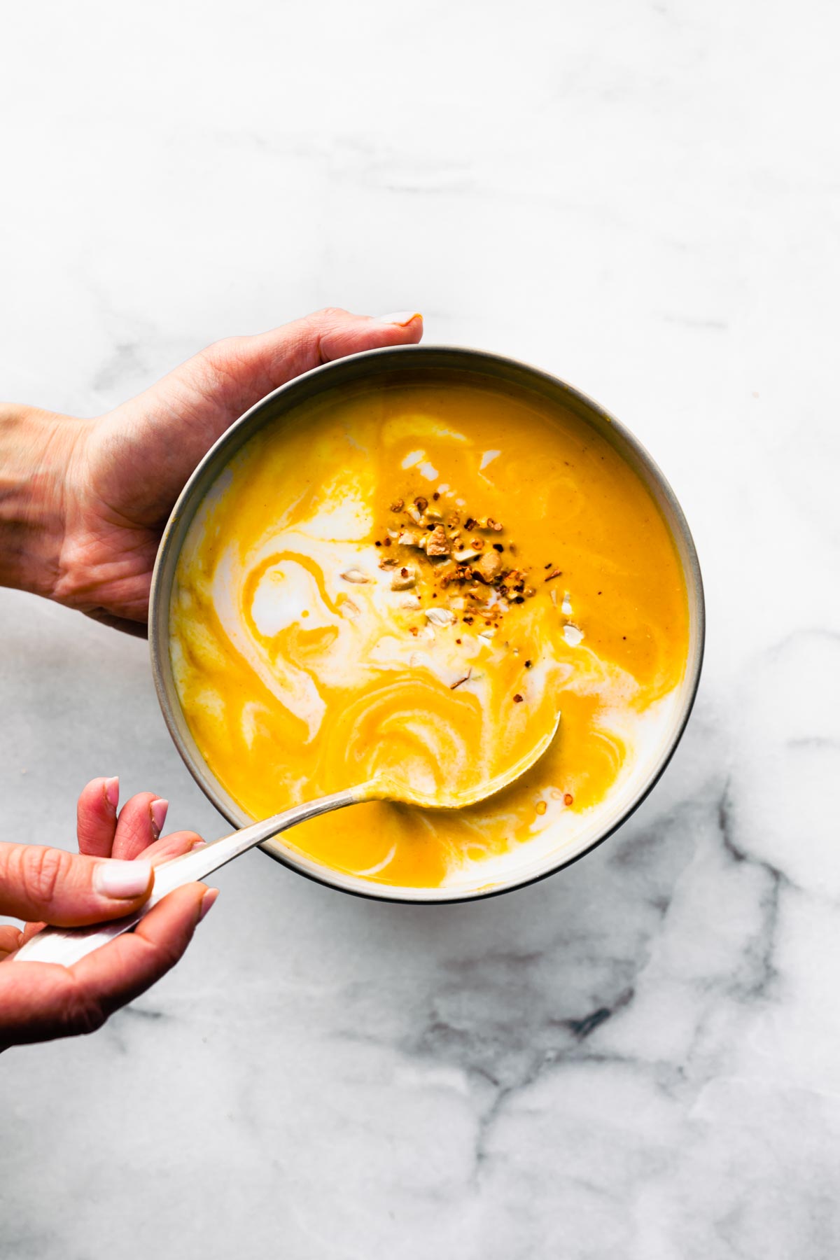 Overhead photo of a woman's hands holding and eating carrot ginger soup with a spoon.