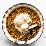 Baked gluten free apple crisp topped with vanilla ice cream and two serving spoons.