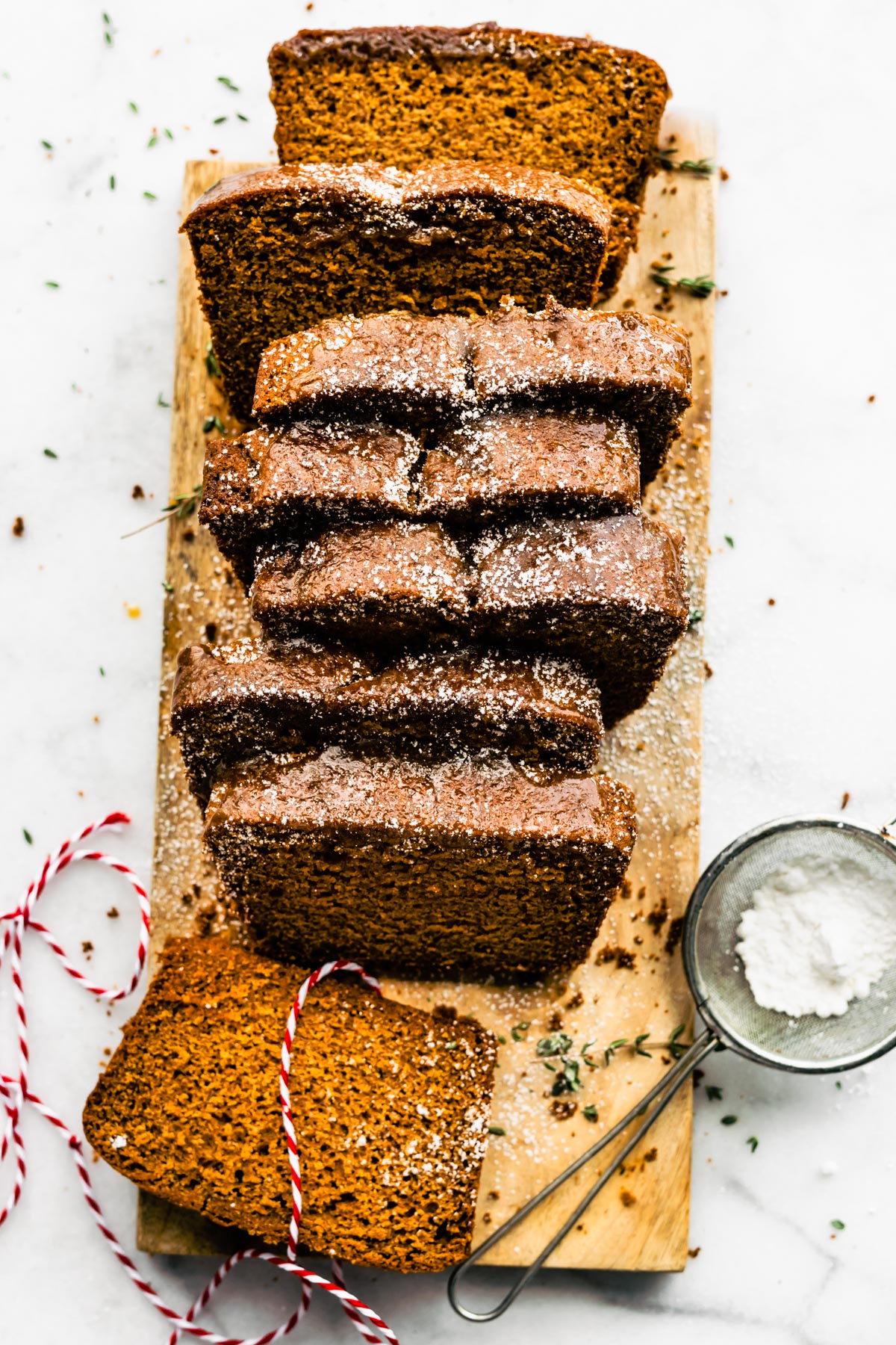Overhead photo of sliced gingerbread loaf on a wooden cutting board sprinkled with powdered sugar.