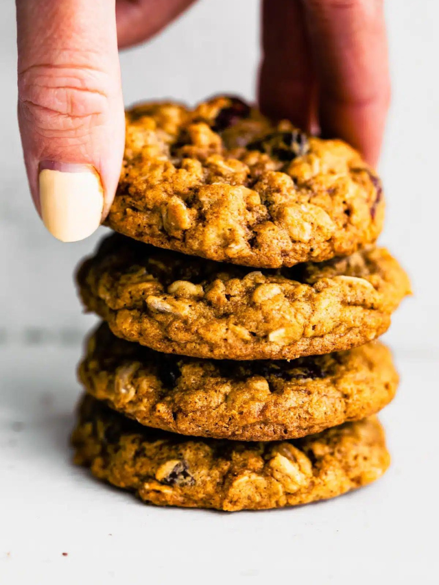 A woman's hand grabbing a gluten free oatmeal cookie from a stack of four cookies.